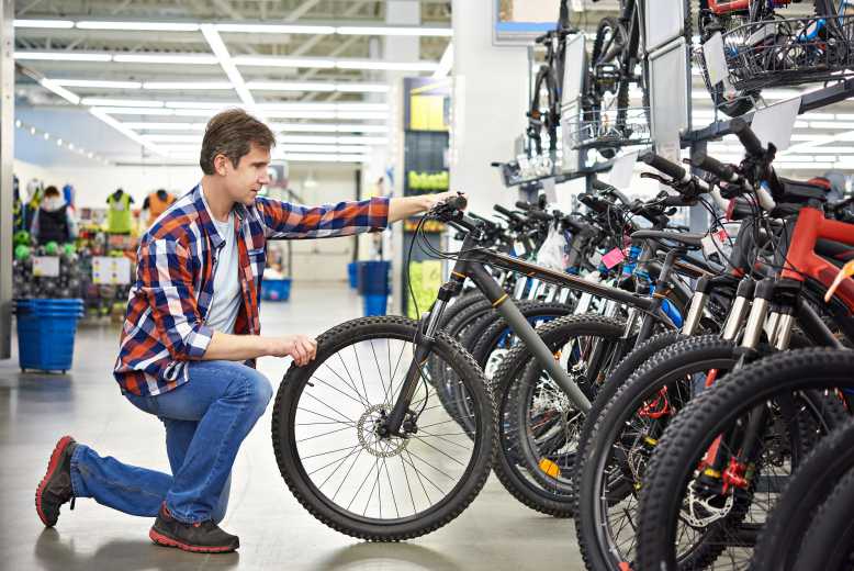 Père avec un adolescent demandant de l'aide à une vendeuse positive pour un magasin de vélo de sport