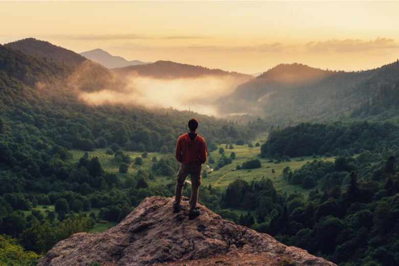 Jeune homme debout sur la falaise en été, dans les montagnes, au coucher du soleil, et bénéficiant d'une vue sur la nature