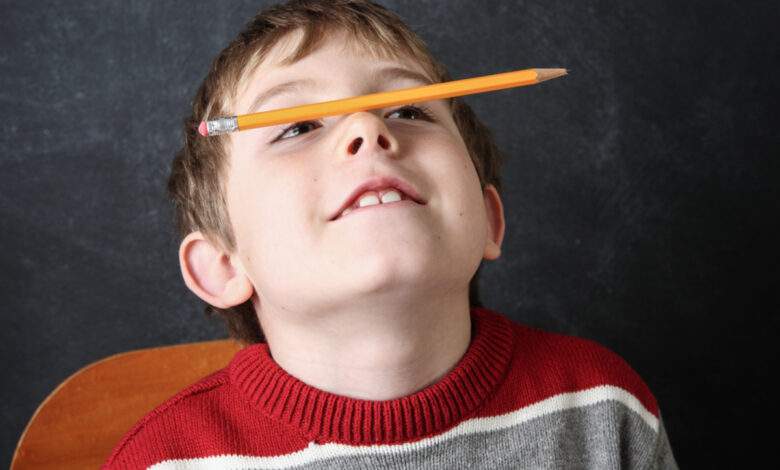 Jeune garçon qui fait le clown avec un crayon en équilibre sur son nez.