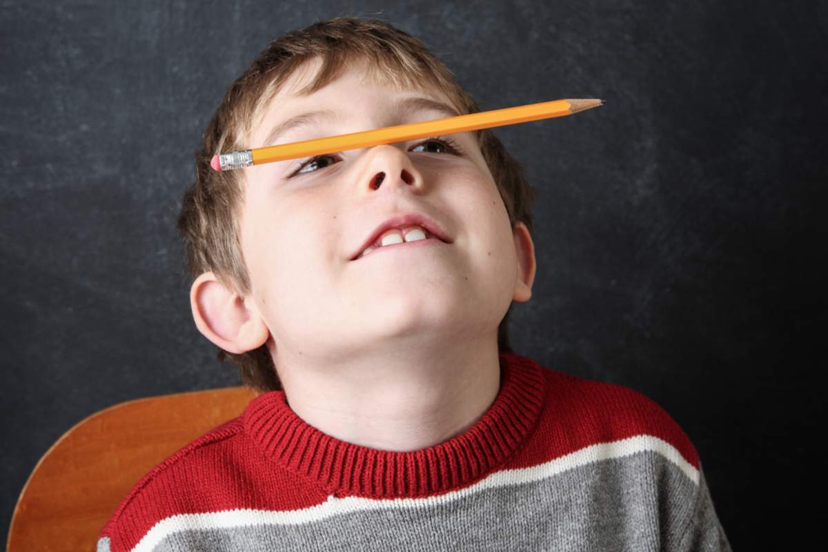 Jeune garçon qui fait le clown avec un crayon en équilibre sur son nez.