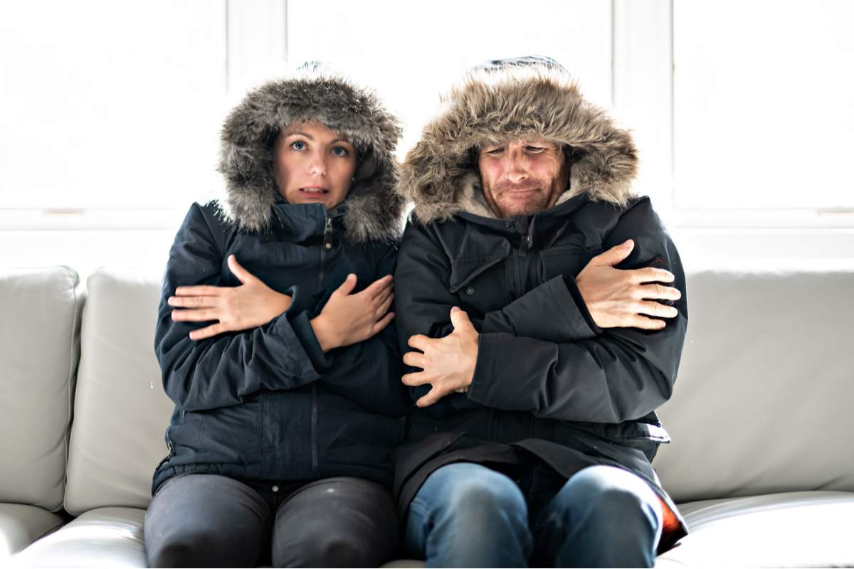 Les couples ont froid sur le canapé à la maison avec leur manteau d'hiver