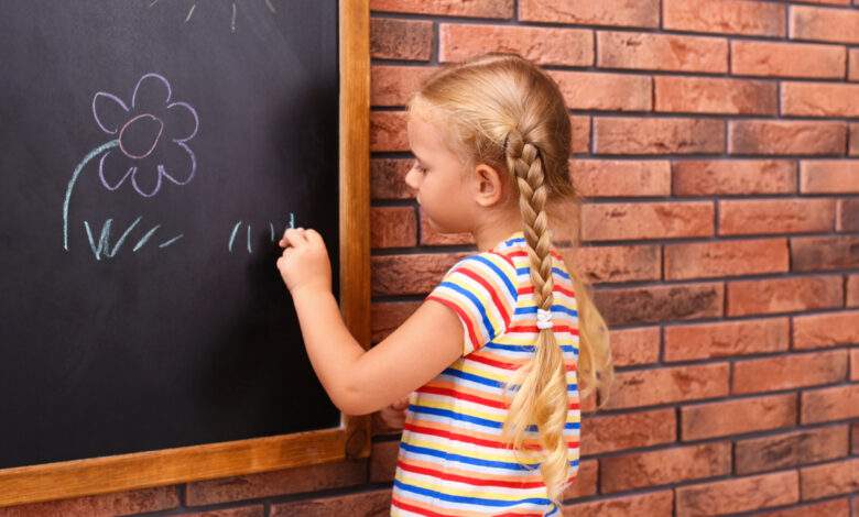 Petite fille gauchère dessinant sur un tableau près du mur de briques