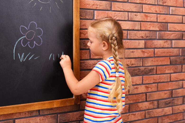 Petite fille gauchère dessinant sur un tableau près du mur de briques