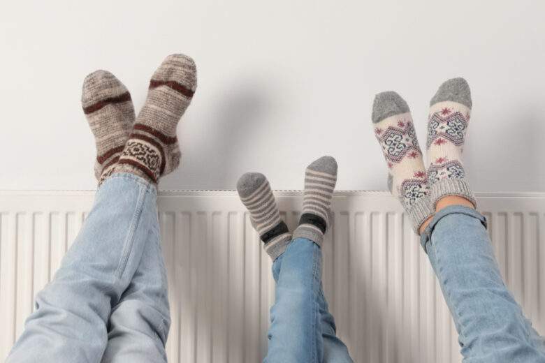 3 paires de pieds posés sur un radiateur près d'un mur blanc