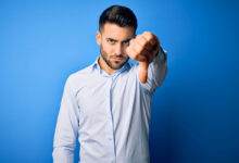 Jeune homme portant une chemise élégante montrant le rejet et le geste négatif avec le pouce gauche vers le bas