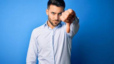 Jeune homme portant une chemise élégante montrant le rejet et le geste négatif avec le pouce gauche vers le bas