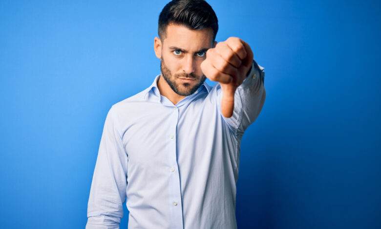 Jeune homme portant une chemise élégante montrant le rejet et le geste négatif avec le pouce gauche vers le bas