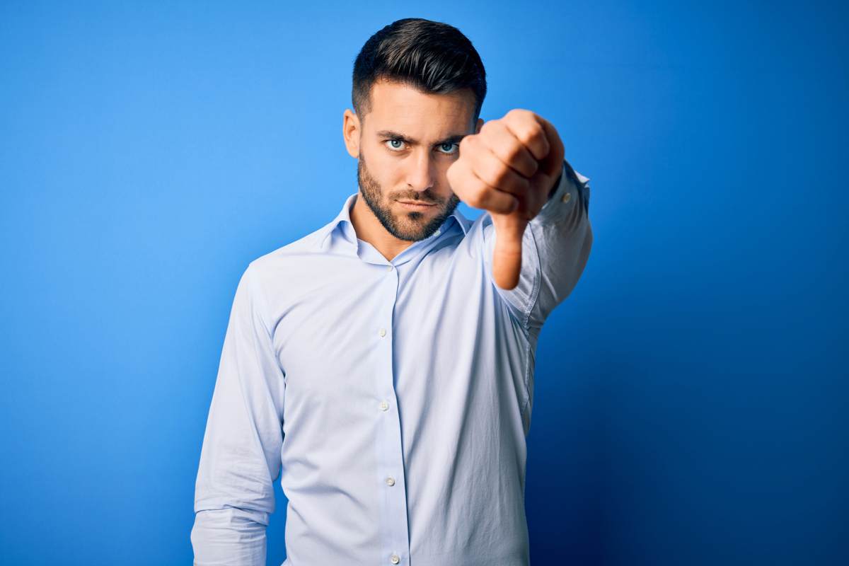 Jeune homme portant une chemise élégante montrant le rejet et le geste négatif avec le pouce gauche vers le bas