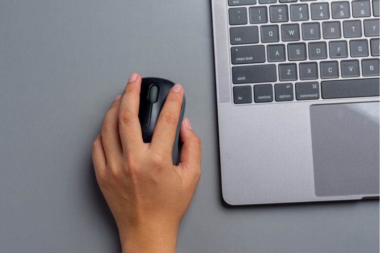 une femme travaille avec un ordinateur portable à la maison et tient une souris d'ordinateur dans sa main gauche.