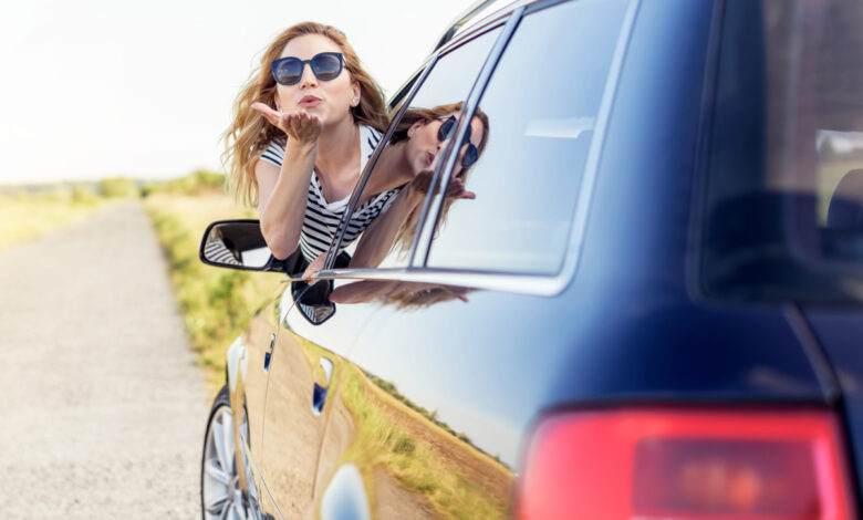 Une jolie femme souriante envoie un baiser aérien depuis la fenêtre de la voiture