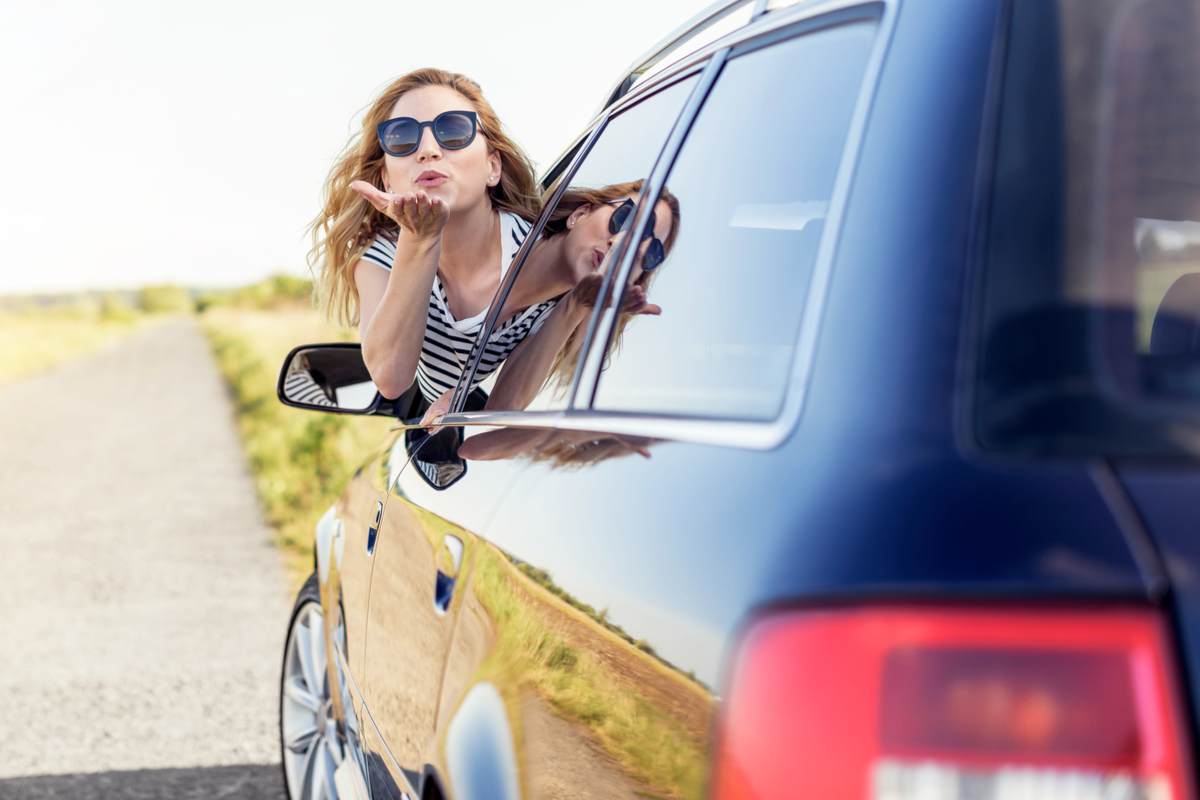 Une jolie femme souriante envoie un baiser aérien depuis la fenêtre de la voiture