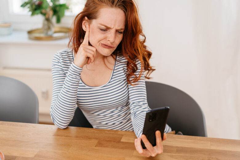 Une jeune femme perplexe ou confuse en train de grimacer sur son téléphone en lisant un texto