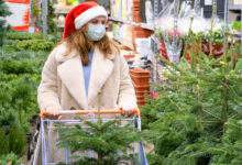 Une femme en chapeau de Père Noël et masque médical choisit un arbre de noël dans le magasin avec des cadeaux de nouvelle année
