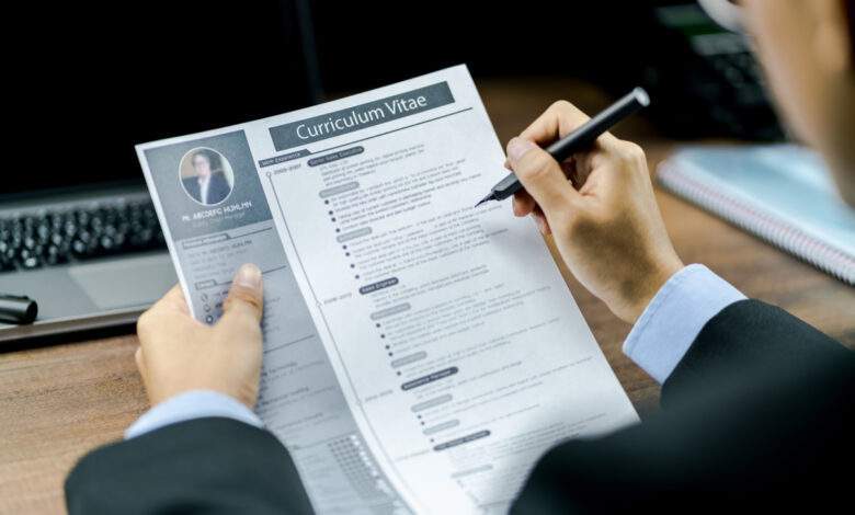 Homme d'affaires utilisant le stylo pour examiner ou vérifier le curriculum vitae ou le CV du candidat avant d'interviewer avec un ordinateur portable et un téléphone sur la table en bois en arrière-plan