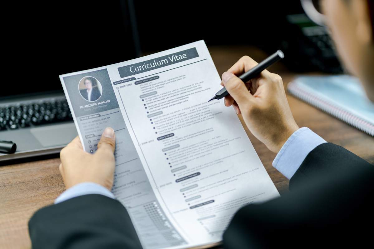 Homme d'affaires utilisant le stylo pour examiner ou vérifier le curriculum vitae ou le CV du candidat avant d'interviewer avec un ordinateur portable et un téléphone sur la table en bois en arrière-plan