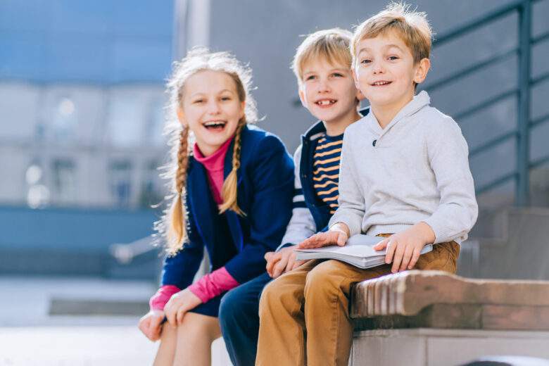  Trois enfants d'âge différents avec un livre assis sur le banc de la cour de récréation 