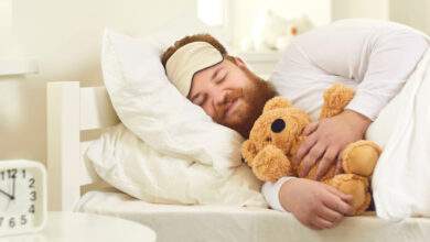 Joyeux homme adulte dormant dans un bon lit confortable avec un mignon ours en peluche
