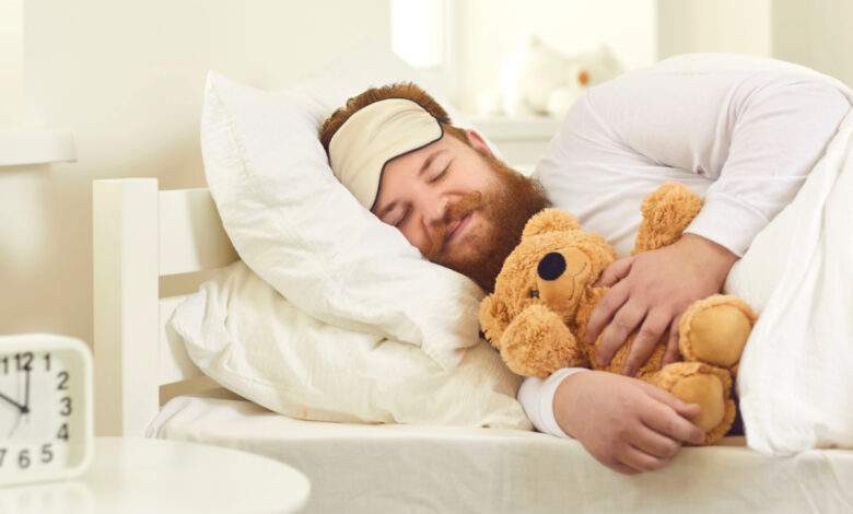 Joyeux homme adulte dormant dans un bon lit confortable avec un mignon ours en peluche