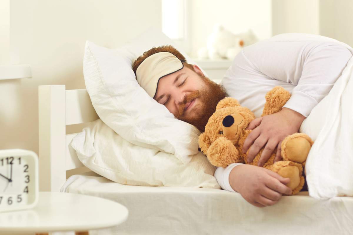 Joyeux homme adulte dormant dans un bon lit confortable avec un mignon ours en peluche
