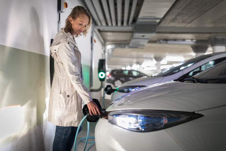 Jeune femme chargeant un véhicule électrique dans un garage souterrain équipé d'un chargeur de voiture
