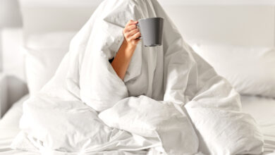 Une femme sous une couette blanche avec une tasse