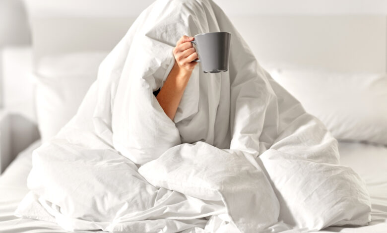 Une femme sous une couette blanche avec une tasse