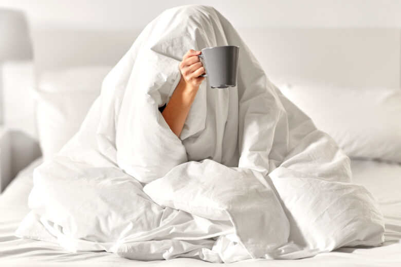 Une femme sous une couette blanche avec une tasse