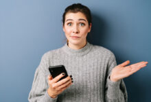une femme avec un pull qui tient un téléphone en faisant la grimace