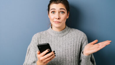 une femme avec un pull qui tient un téléphone en faisant la grimace