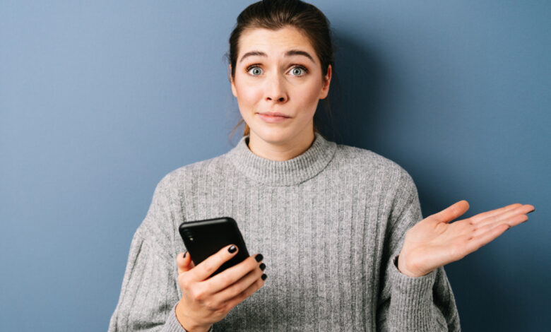 une femme avec un pull qui tient un téléphone en faisant la grimace