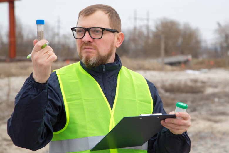 Un homme avec un gilet jaune et des lunettes fait une analyse de sol