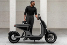 Un homme habillé en noir devant le scooter électrique Naon Zero-One