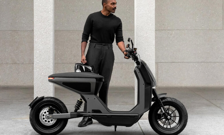 Un homme habillé en noir devant le scooter électrique Naon Zero-One