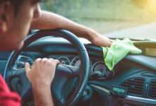 un homme nettoie le tableau de bord de sa voiture avec un chiffon vert