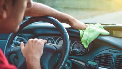 un homme nettoie le tableau de bord de sa voiture avec un chiffon vert