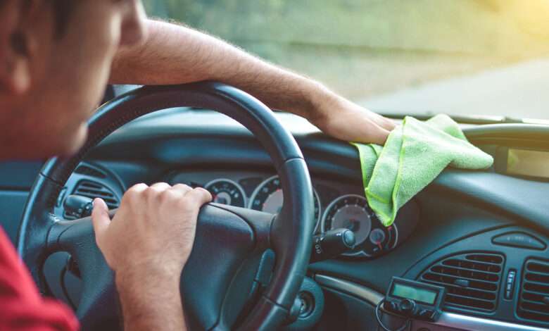 un homme nettoie le tableau de bord de sa voiture avec un chiffon vert