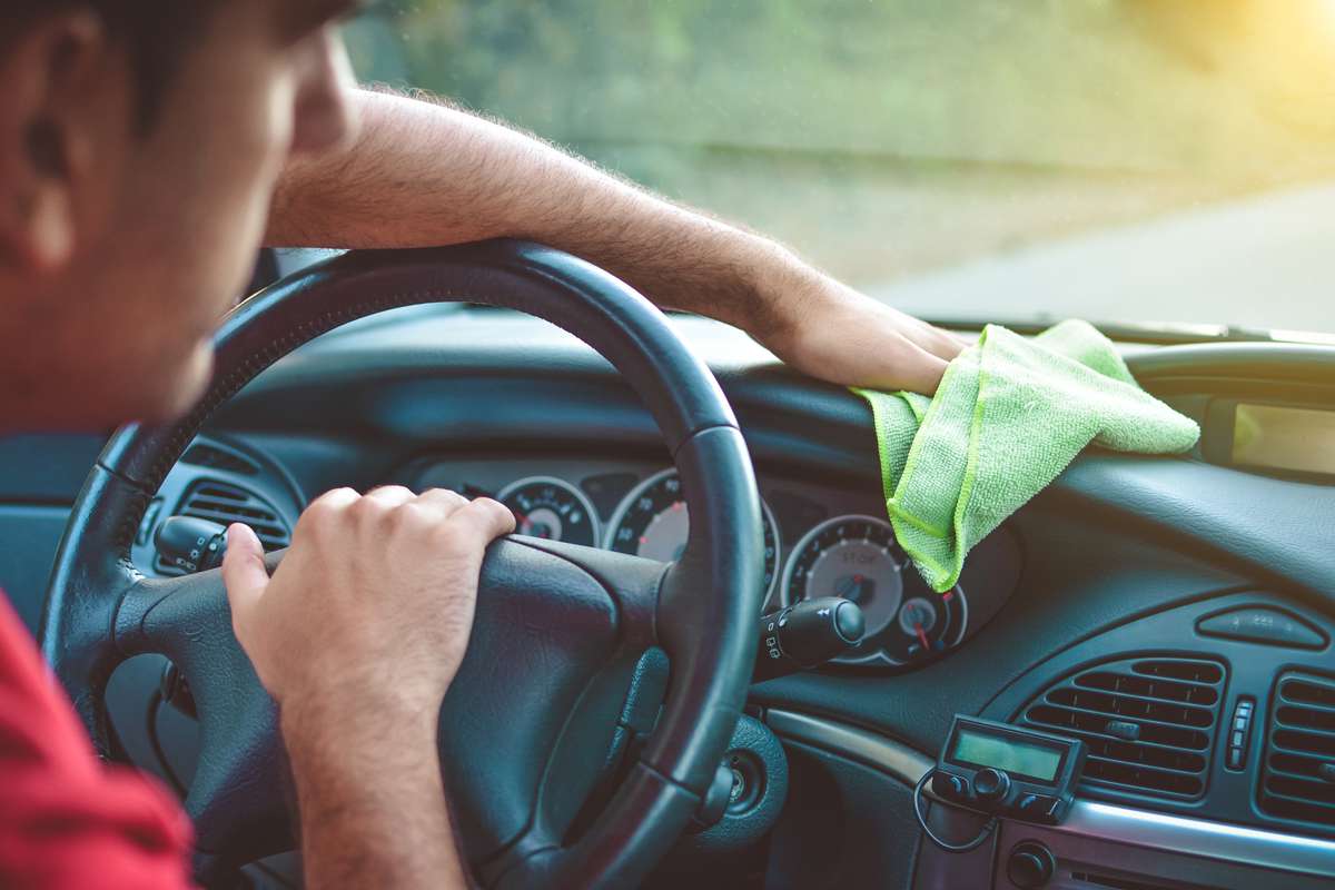 un homme nettoie le tableau de bord de sa voiture avec un chiffon vert