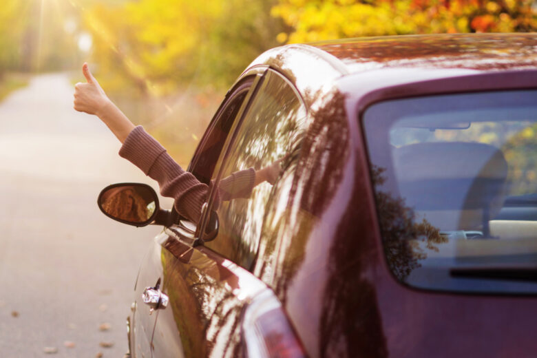 Une femme qui passe le bras par la fenêtre de sa voiture le pouce en l'air