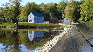 Une maison passive bleue au bord d'un lac avec des panneaux solaires.