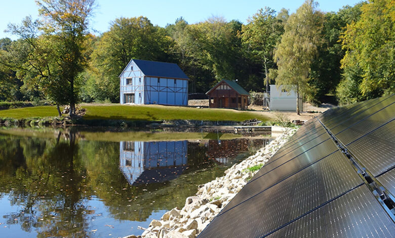 Une maison passive bleue au bord d'un lac avec des panneaux solaires.