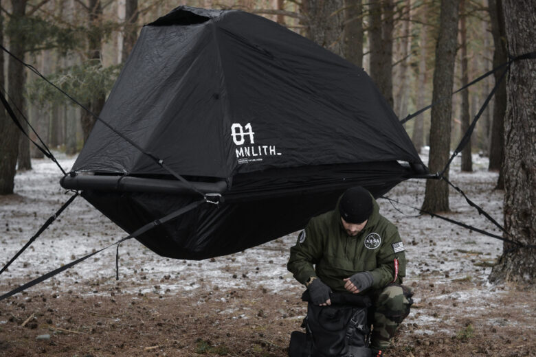 Un homme devant une tente suspendue dans la forêt
