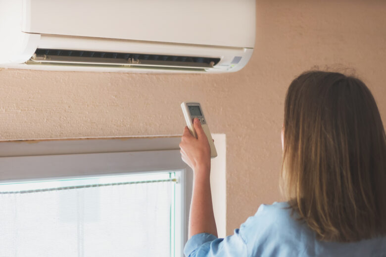 Femme tenant la télécommande visant le climatiseur.