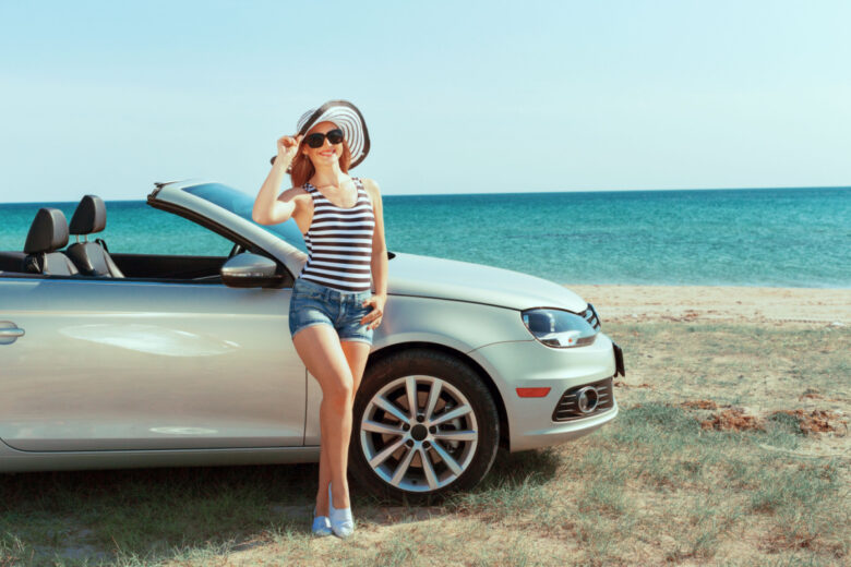 Une femme devant une voiture devant la mer. 