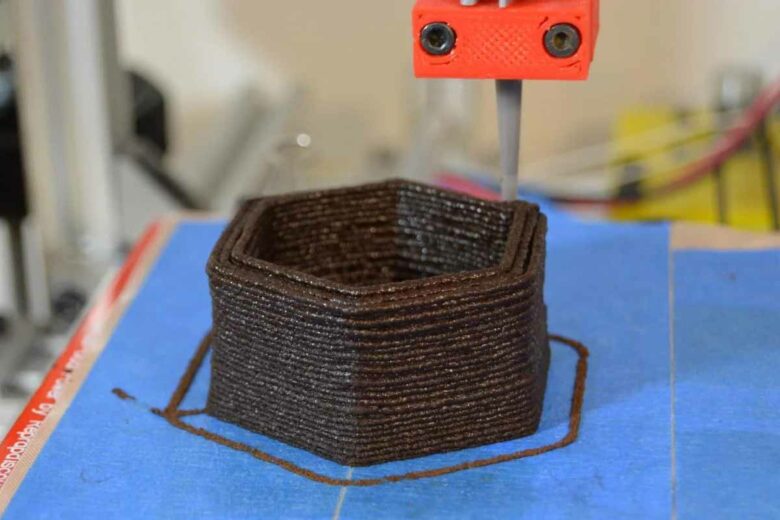 Une imprimante 3D dépose des couches d'un matériau à base de marc de café usagé pour fabriquer un pot de fleurs.