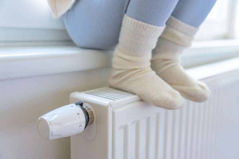 Une enfant se réchauffant les pieds sur un radiateur.