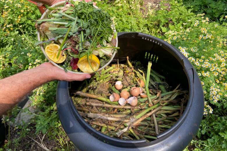 Une personne qui jette ses déchets dans un composteur de jardin.