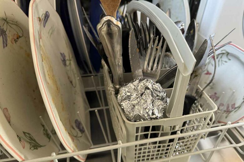Une boule de papier aluminium dans le bac à couverts du lave-vaisselle.