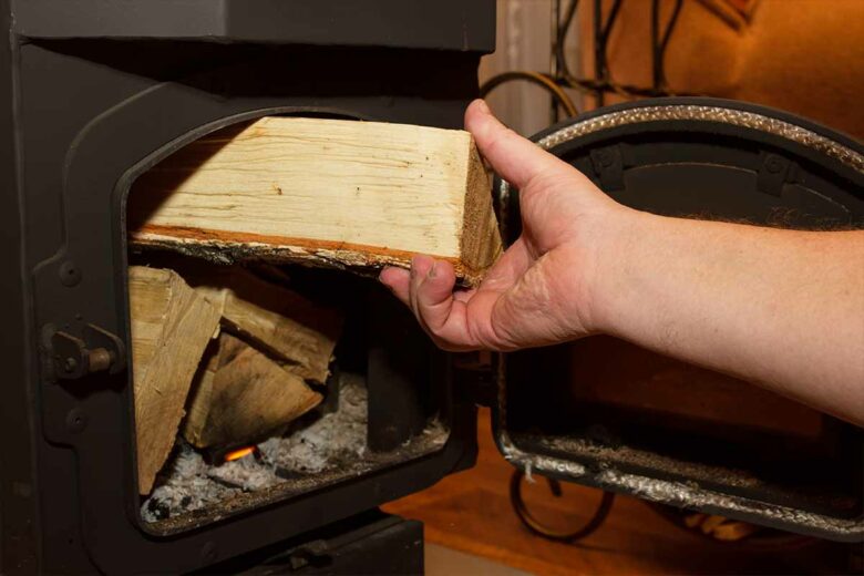 Une personne qui charge son poele à bois avec des buches.