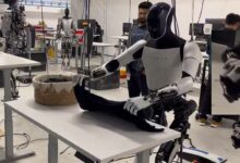 Le robot Optimus de Tesla pliant du linge, on distingue sur la droite la main d'un opérateur contrôlant cette tâche.