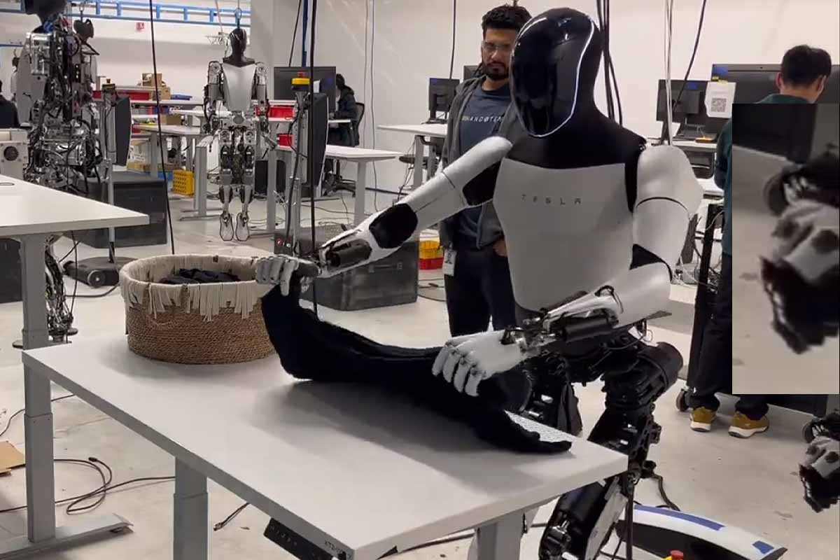 Le robot Optimus de Tesla pliant du linge, on distingue sur la droite la main d'un opérateur contrôlant cette tâche.